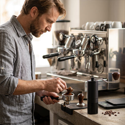 Bariste chargeant un porte-filtre de café fraîchement moulu à côté d'une machine expresso professionnelle et du moulin a cafe compact | Le Pommeau.