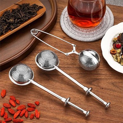 Boule à thé | Infusion Élégante - modèles à poussoir et à pince sur une table en bois avec thé en vrac