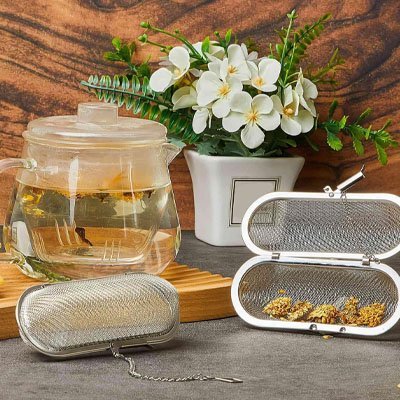 Boule à Thé | Inox Perfect ouvert montrant du thé en vrac à côté d'une théière en verre et d'un pot de fleurs blanches