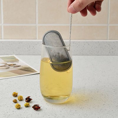 Boule à Thé | Inox Perfect plongeant dans un verre d'eau chaude dorée, fleurs de thé séchées à cöté.