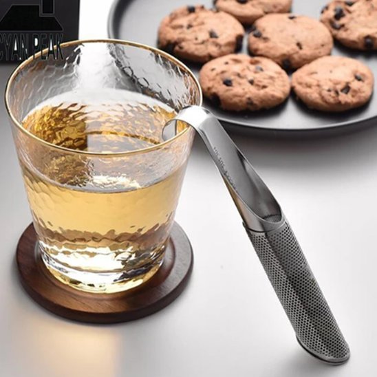 Cuillère à thé | Élégance Inox - suspendue au bord d'un verre d'eau chaude martelé. Une assiette de cookies aux pépites de chocolat est visible en arrière-plan