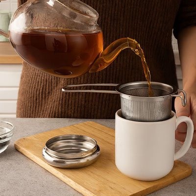 Infuseur à thé en inox 304 poignées doubles dans une tasse blanche avec son socle d'égouttement