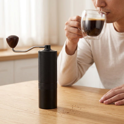 Moulin a cafe | Le Pommeau sur une table en bois avec un homme buvant son café en arrière-plan.