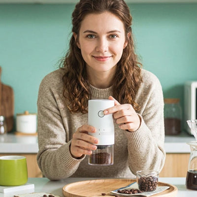 Moulin à café rechargeable blanc tenu de face par une femme souriante.