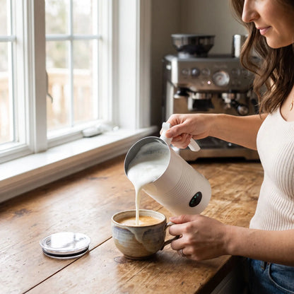 Mousseur à lait électrique Le Mousséat blanc mousse octueuse versée dans un espresso par une femme