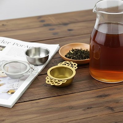 Passoire à thé Arabesque à côté d'une carafe remplie de thé infusé