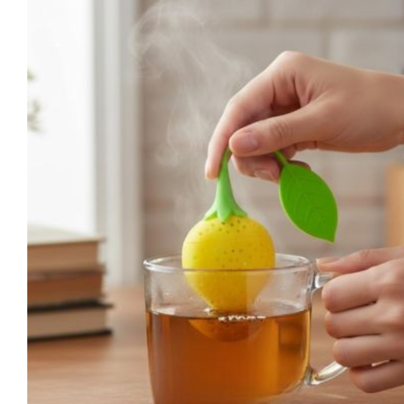 Plan rapproché d'une main abaissant un Infuseur a Thé | Fraisinette jaune vif dans une tasse en verre