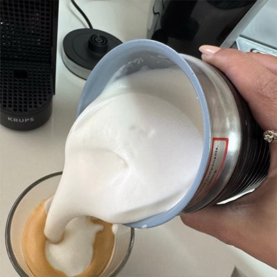 Vue rapprochée d'un utilisateur versant une mousse onctueuse et dense depuis un mousseur à lait électrique dans une tasse de café.